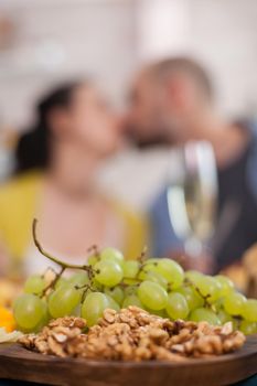 Close up of white grapes on wooden plates with nuts on wooden plate and couple kissing in the background.