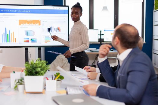 African leader briefing business organization pointing at graph briefing teamwork. Corporate staff discussing new business application with colleagues looking at screen