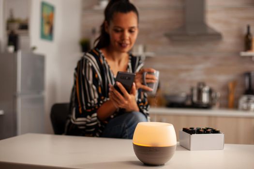 Woman watching video on phone and enjoying steam with essential oils from diffuser. Aroma health essence, welness aromatherapy home spa fragrance tranquil theraphy, therapeutic steam, mental health treatment