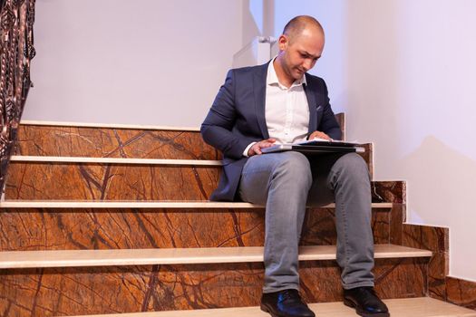 Exhausted tired businessman reading professional deadling financial raport. Entrepreneur working late in evening corporate sitting on stairs in building office.