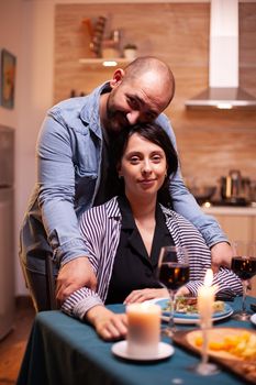 Couple celebrating relationship looking at webcam in kitchen. Married people special tender moments, enjoying the meal at candle lights celebration.