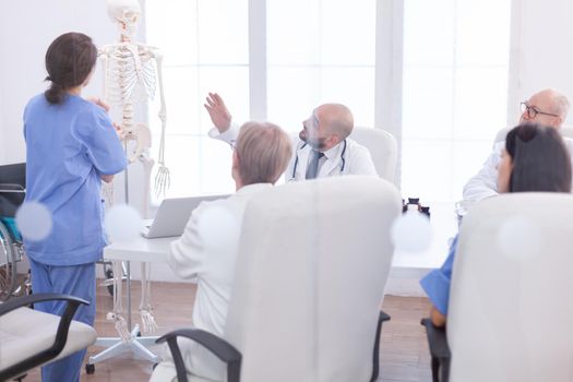 Expert doctor in radiology pointing at human skeleton during presentation in hospital conference room. Clinic therapist talking with colleagues about disease, medicine professional.