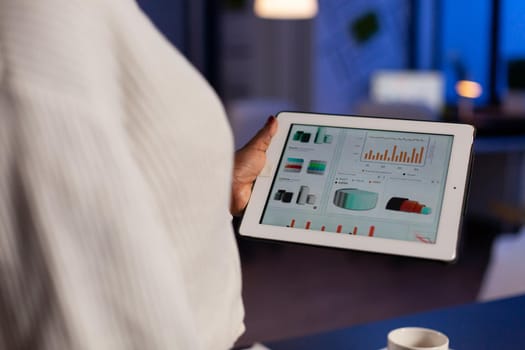 Close up of overworked black manager checking graph documents on tablet pc. Busy african employee analysing financial statistics in workplace overworking writing, searching.