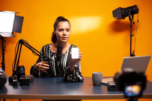 Filmmaker showing mini led light while recording podcast. Video blogger recording a vlog with technology product equipment use in videography and photography.