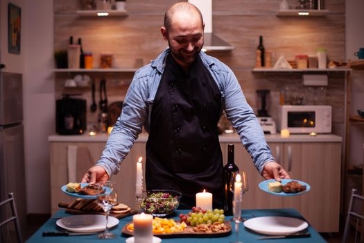 Husband holding plates with food for romantic dinner in dining room with wife. Man preparing festive dinner with healthy food, cooking for his woman a romantic dinner,