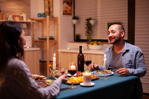 Husband telling a story to wife in kitchen during festive dinner. Relax happy people, sitting at table in kitchen, enjoying the meal, celebrating anniversary in the dining room