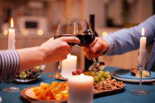 Lovers clink wine glasses in dining room for relationship anniversary. Happy cheerful young couple dining together in the cozy kitchen, enjoying the meal, celebrating anniversary romantic toast