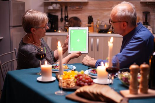 Green screen tablet at dinner. Aged people looking at green screen template chroma key display sitting at the table in kitchen during dinner.