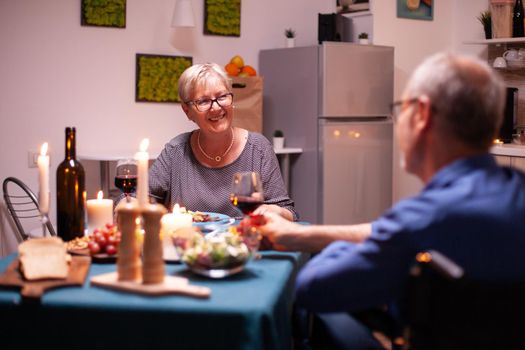 Old woman smiling at disabled husband in wheelchair during dinner.