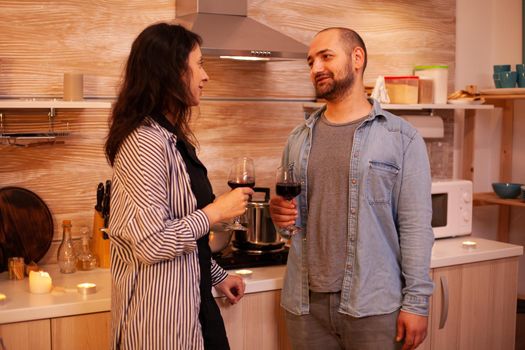 Man and woman having fun during date drinking wine. Adult couple having romantic date at home, in the kitchen, talking, smiling, enjoying the meal in dining room.