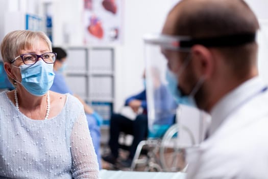 Close up of senior woman with face mask against covid pandcemic during consultation with doctor in hospital room. Global health crisis, medical system , sick elderly patient in private clinic.