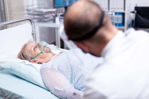 Senior woman breathing with oxygen mask laying on bed during pulmonary treatment for coronavirus. Medicine medical healthcare system epidemic lungs infection treatment