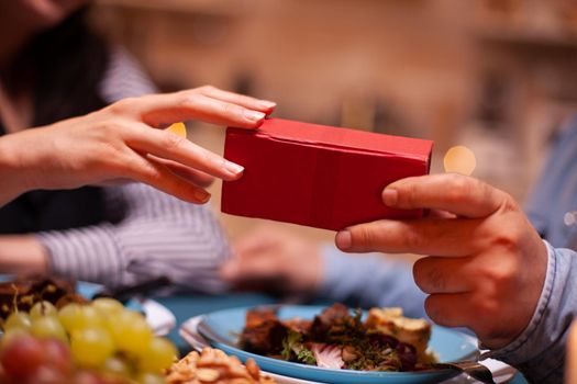 Close up of present box and couple having romantic dinner. Cheerful man dining with woman at home, enjoying the meal, celebrating their anniversary at candle lights.