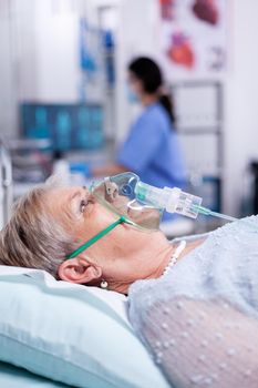 Oxygen mask helping old woman breath while laying in hospital bed because of infection with coronavirus. Medicine medical healthcare system epidemic lungs infection treatment