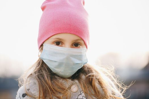 Sick girl wearing protection during pandemic. Pretty young Caucasian girl taking on medical mask outdoor. Girl Wearing Medical Mask During Coronavirus COVID-19 Epidemic