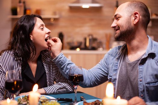 Wife and husband celebrating anniversary with red wine, tender moments at candle lights in kitchen. Delicious grapes.