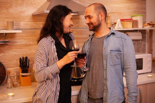 Couple smiling at each other during their romantic date in kitchen. Adult couple at home, drinking red wine, talking, smiling, enjoying the meal in dining room.