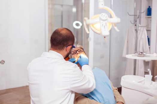 Denstis in cabinet repairing senior patient tooth in dental clinic. Elderly patient during medical examination with dentist in dental office with orange equipment.