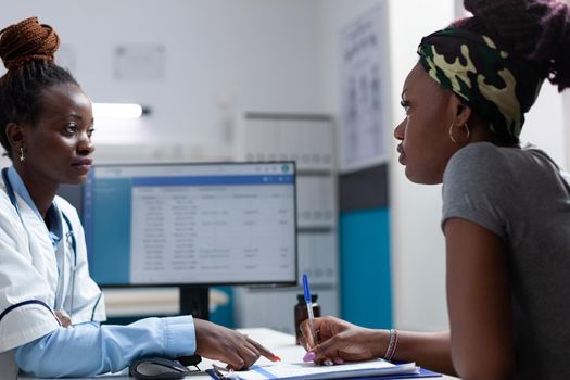 African american therapist doctor explaining healthcare treatment to sick patient while signing medical documents during clinical appointment in hospital office. Disease results papers