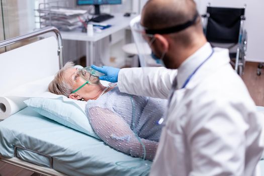 Doctor putting oxygen mask on senior woman laying in hospital during coronavirus pandemic. Patient breathing heavily. Medicine medical healthcare system epidemic lungs infection treatment