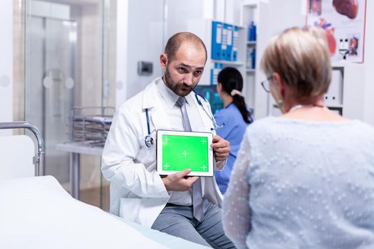 Doctor with green screen tablet in front of elderly patient explaining medical diagnosis. Ready chroma mockup for your app, text, video or other digital asset