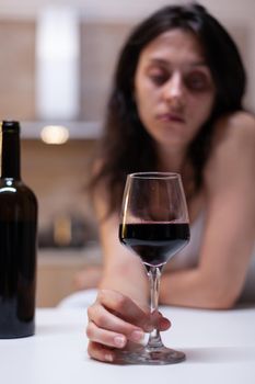 Close up of glass and bottle filled with wine for woman feeling lonely and heartbroken at home. Depressive alcohol addict holding beverage drinking alone. Emotional person intoxicated