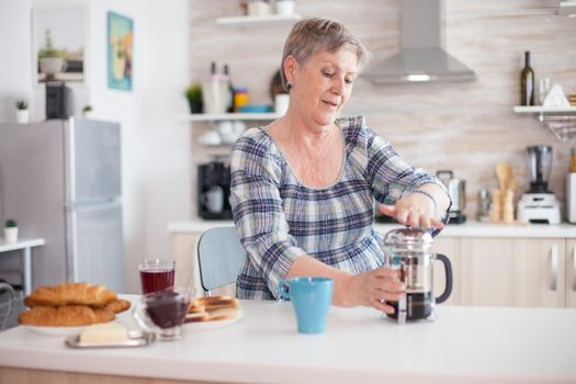 Senior woman enjoying a mug of coffee from french press during breakfast. Elderly person in the morning enjoying fresh brown cafe espresso cup caffeine from vintage mug, filter relax refreshment