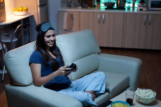 Gamer using joystick playing video games on console sitting on couch in living room. Excited determined woman using controller gamepad keypad playstation gaming and having fun winning electronic game