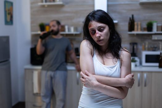 Depressed bruised woman being victim of domestic violence, aggression and alcohol addiction from violent drunk man. Couple with physical abuse problems, wife with bruises, alcoholic husband