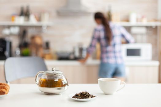Woman preparing breakfast in kitchen and aromatic herbs for hot tea. Shot with background blur of lady having great morning with tasty natural healthy herbal tea sitting in the kitchen.