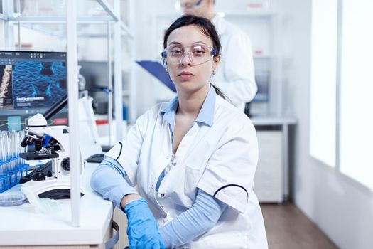 Portrait of successful scientist in microbiology laboratory wearing protection equipment. Chemist wearing lab coat using modern technology during scientific experiment in sterile environment.