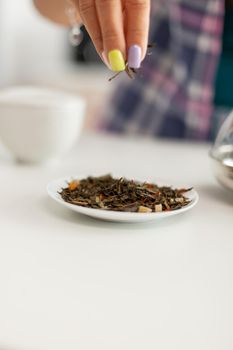 Close up of housewife hand while preparing green tea in the morning Doing tea in a modern kitchen sitting near the table. Putting with hands, healthy herbal in pot.