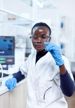 African biochemistry looking at sample on glass slide with protection glasses during medical investigation. Black healthcare scientist in biochemistry laboratory wearing sterile equipment.