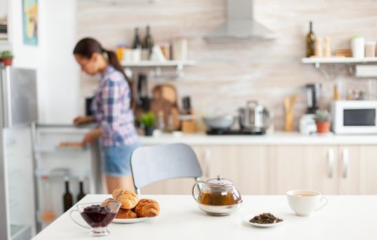 Woman looking into refrigerator for food to prepare breakfast in kitchen. Shot with background blur of lady having great morning with tasty natural healthy herbal tea.