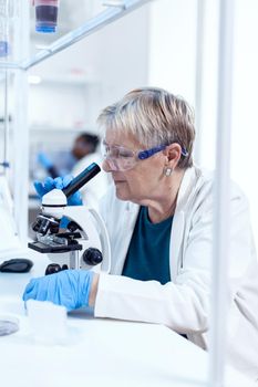 Concentrated senior scientist conducting genetic experiment using microscope. Elderly researcher carrying out scientific research in a sterile lab using a modern technology.