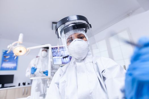 Patient pov of dentist holding dental tools wearing covid protection treating patient. Stomatolog wearing safety gear against coronavirus during heatlhcare check of patient.