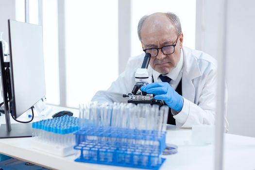 Healthcare senior scientist man in medical industry carrying out genetic analysis using microscope. Chemist researcher in sterile lab doing experiments for medical industry using modern technology.