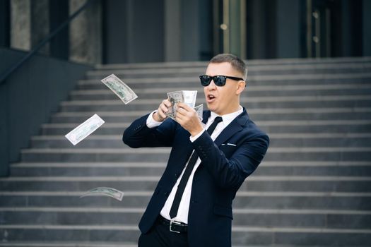 Successful business or winning the lottery. Money rain, falling dollars. Portrait shot of cheerful rich handsome businessman in glasses and suit throws money. Happy good looking man throwing dollars.