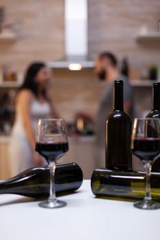 Close up of empty bottles of alcoholic beverage and glasses with wine on kitchen counter. Liquor and booze prepared for intoxicated couple with alcohol addiction sitting in background