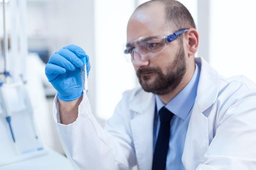 Concentrated scientist in laboraty conducting sample reseach. Researcher in biotechnology sterile lab holding analysis in tube wearing gloves and protection glasses.
