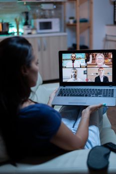 Back view of woman using laptop on videocall sitting on comfortable couch. Remote worker having online meeting consulting with colleagues on video conference and webcam chat using internet technology.