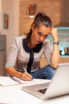 Concentrated freelance woman working overtime to finish a project from home kitchen. Employee using modern technology at midnight doing overtime for job, business, career, network, lifestyle ,wireless.