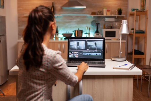 Back view of creative filmmaker working on a movie on laptop during midnight. Content creator in home working on montage of film using modern software for editing late at night.