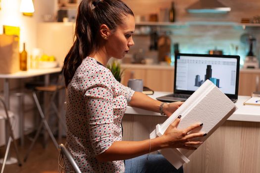 Female architect looking at building model during late night time in home office. Engineer artist creating and working in office holding scale building model, determination, career.