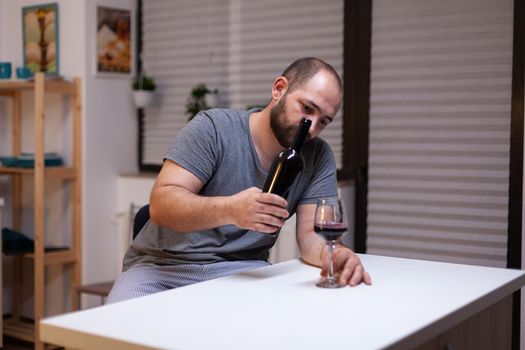 Lonely man pouring wine in glass from bottle drinking alone feeling depressed and unhealthy. Miserable adult with alcohol addiction being intoxicated with liquor, booze, beverage