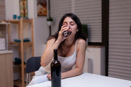 Unhappy woman with alcohol addiction drinking wine alone feeling depressed and intoxicated. Young adult with bottle of wine and glass using liquor for sadness, loneliness and desperation