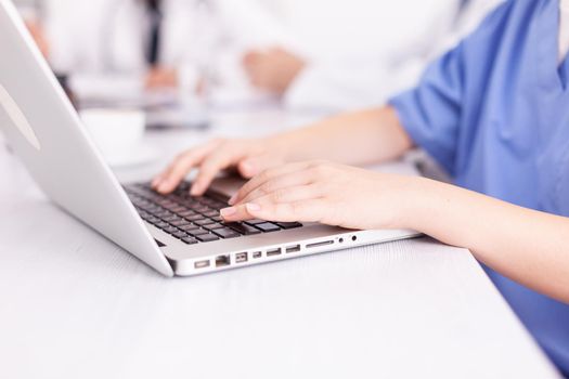 Close up of medical nurse typing on laptop during healtchare meeting with coworkers in hospital boardroom. Clinic expert therapist talking with colleagues about disease, medicine professional