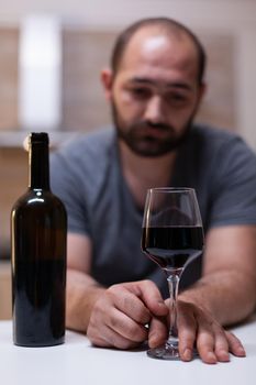 Close up of glass with wine for lonely man in kitchen. Miserable adult having bottle of alcohol drinking while being alone and stressed. Person with liquor, booze and alcoholic beverage