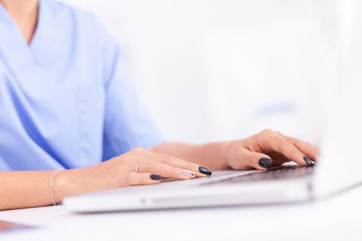 Close up of physician in hospital office typing patient diagnosis. Health practitioner searching in hospital database using laptop in hospital cabinet, keyboard, job.