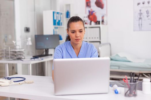 Medical practitioner typing patient health report on laptop in hospital office. Health care staff sitting at desk using computer in modern clinic looking at monitor, medicine.